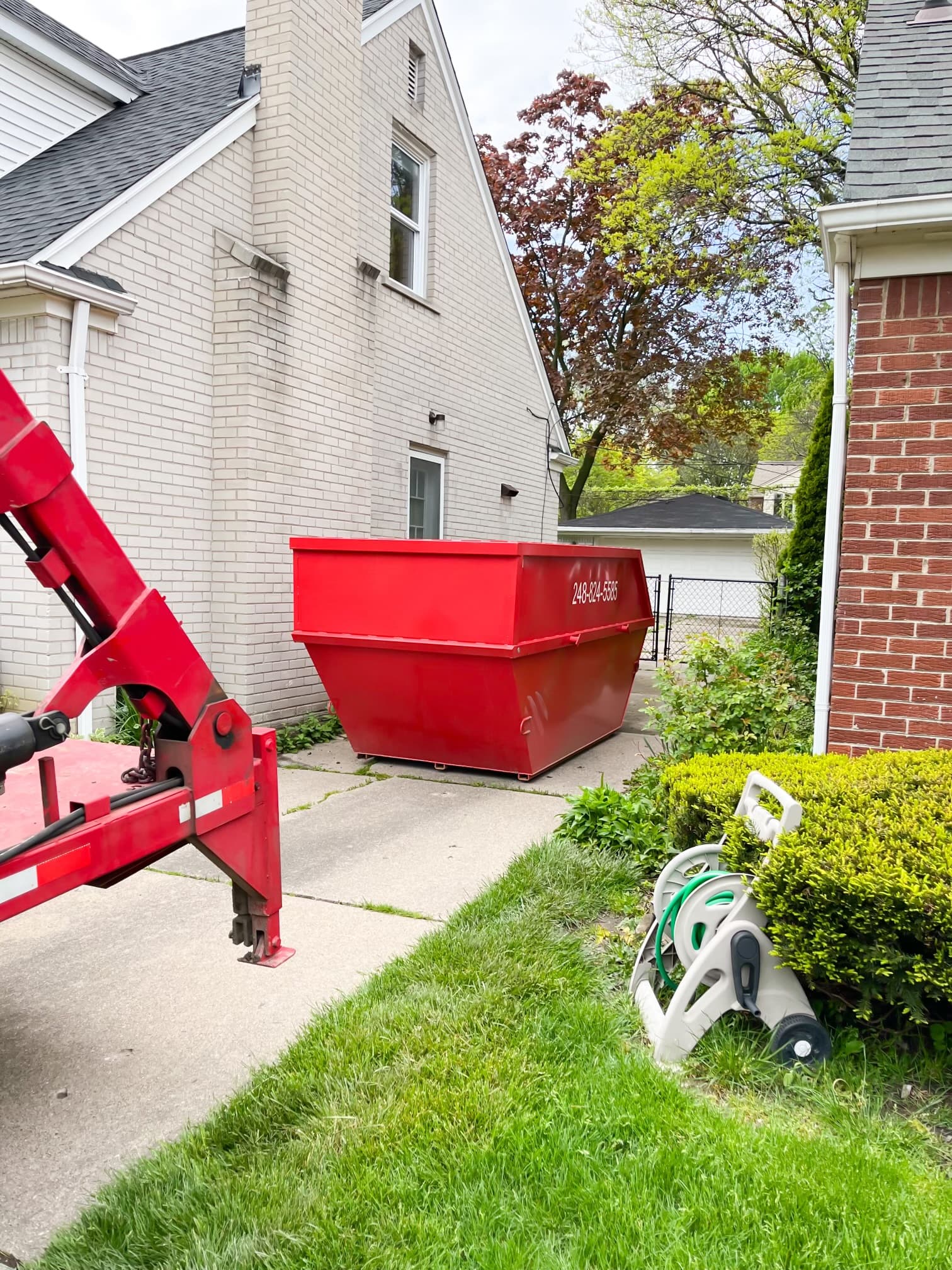A red Red-E-Bins dumpster delivered beside a brick home